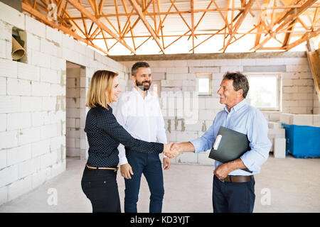 Young couple with architect or civil engineer looking at plans of their new house, discussing issues at the construction site. Stock Photo