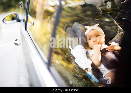 Cute little baby girl fastened with security belt in safety car seat. Shot through glass. Stock Photo