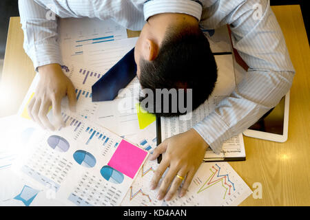executive businessman work hard and  so tired he sleep on working table down use computer tablet with graph chart on analysis data table Stock Photo