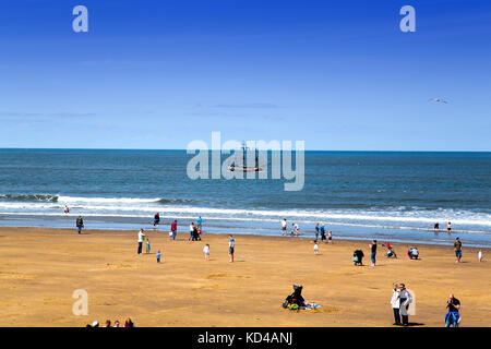 view of people on beach & pleasure boat on a sunny Summers day in Whitby North East Yorkshire UK Stock Photo