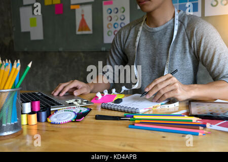 young male fashion designer work with fabric cloth on the wood table Stock Photo