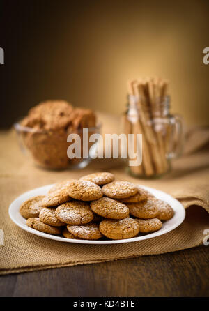 Honey ginger cookies in the foreground. Oatmeal raisin cookies and pirouette rolled wafers in the background.  Burlap on wooden table. Warm home atmos Stock Photo