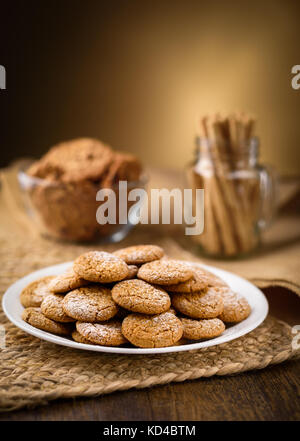 Honey ginger cookies in the foreground. Oatmeal raisin cookies and pirouette rolled wafers in the background.  Jute, burlap on wooden table. Warm home Stock Photo