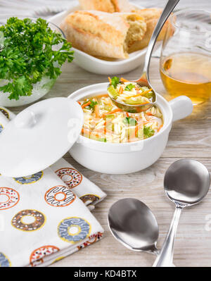 Chicken orzo soup in white crock on wooden background. Italian soup with orzo pasta. Ladle. Bread. Glass of wine. Stock Photo