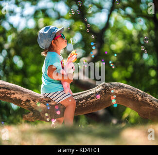 One years old little girl blowing soap bubbles in summer park. Child plaiyng. Stock Photo