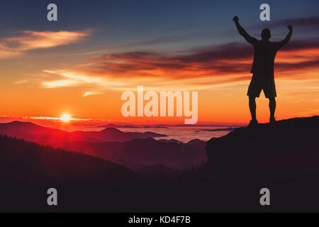 Man silhouette on mountain cliff enjoy panaoramic view. Man watch over misty and foggy morning valley in morning Sun. Stock Photo