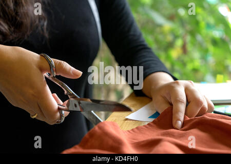 young fashion designer work with fabric cloth on the wood table near the green tree out door Stock Photo