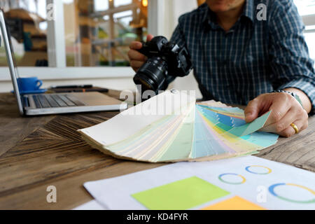 Graphic designer working with computer and color tone paper for choice the best color for the project on wood table work and compare color with camera Stock Photo