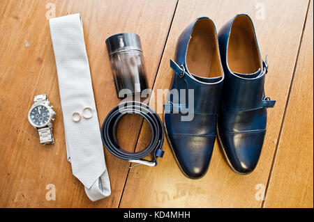 Groom's white tie, silver watch, black leather belt, perfume and a pair of wedding boots. Stock Photo
