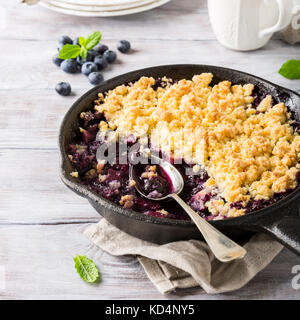 Coconut crumble in cast iron pan with fresh apples and blueberry. Healthy food concept. Stock Photo