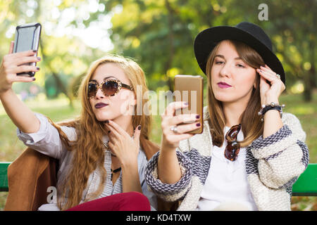 Girls using phones on a park bench Stock Photo