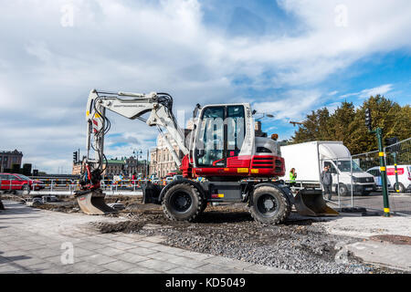 Stockholm, Sweden- October 5, 2017: Red and white excavator in an fenced of part of the street. People in the background Stock Photo