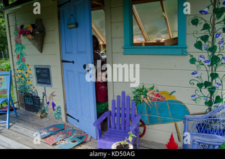 Little girl peeks out door of painted shed in community Garden, Maine USA Stock Photo