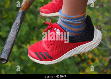 A pair of red youth Adidas sport shoes dangling from the feet of a young person riding a chairlift in Gatineau Park, Quebec, Canada. Stock Photo