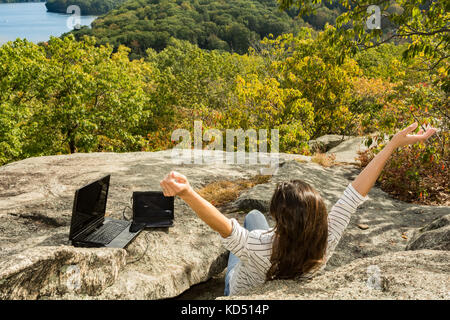 A woman charging her laptop with a solar panel at a remote work location. Stock Photo