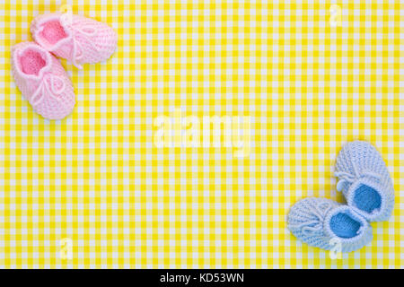 Kinitted Baby booties for a girl and a boy on a yellow gingham background. Stock Photo