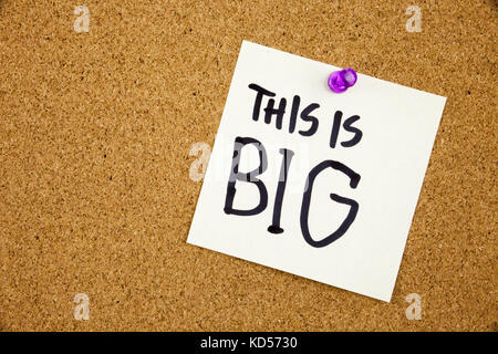 A yellow sticky note writing, caption, inscription Note paper with a text THIS IS BIG and black push pin on cork board. Stock Photo