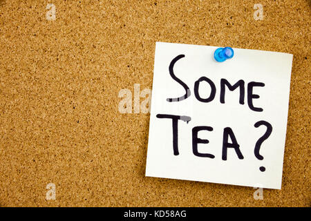 A yellow sticky note writing, caption, inscription Phrase SOME TEA in black ext on a sticky note pinned to a cork notice board Stock Photo