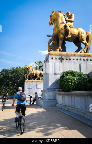 WASHINGTON DC-May 26, 2015: Bike riders approach the east entrance of the Arlington Bridge, under the gilded horse statues topping the bridge gates. O Stock Photo