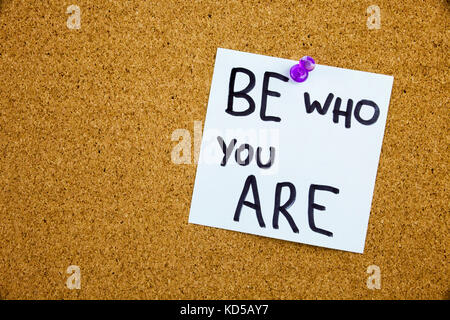 A yellow sticky note writing, caption, inscription chalkboard with the phrase be who are you in black ext on a sticky note pinned to a cork notice board Stock Photo