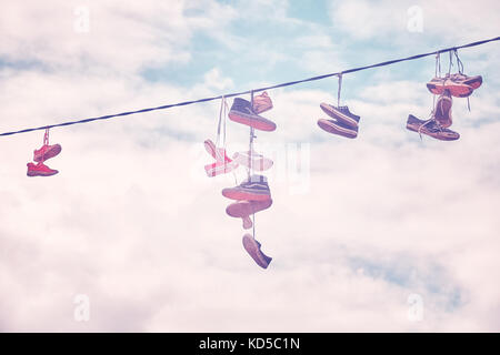 Old shoes hang on wire, color toning applied. Stock Photo