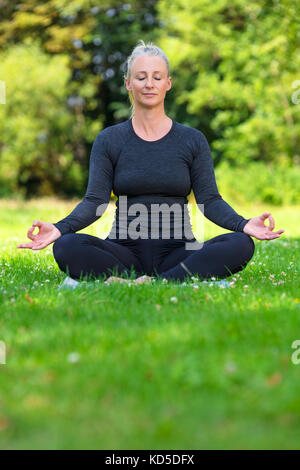 Mature middle aged fit healthy woman practicing yoga kapalbhati pranayama position outside in a natural tranquil green environment Stock Photo