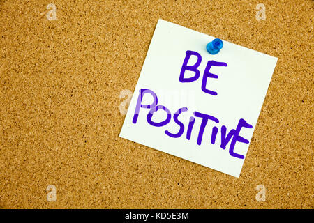 A yellow sticky note writing, caption, inscription be positive, motivational lifestyle reminders against black ext on a colorful sticky note pinned to a cork notice board Stock Photo