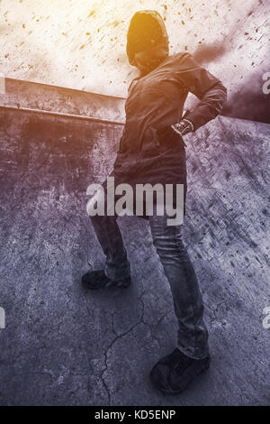 Unrecognizable hooded female person facing concrete wall as ...
