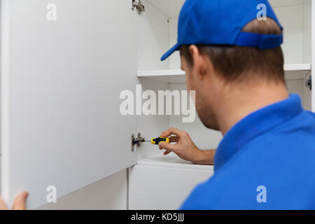 worker in blue uniform doing furniture assembly with screwdriver Stock Photo