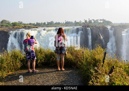 Tourists photographing main falls at Victoria Falls or Mosi-oa-Tunya (the smoke that thunders), Zimbabwe, Southern Africa Stock Photo