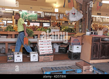 Cleveland West Side Market produce vendor carries carrots to weigh them while a customer waits at the counter inside this landmark building. Stock Photo