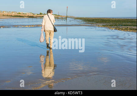 Woman waking on a beach at low tide with a reflection of her in the wet sand. Stock Photo