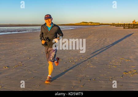 Man smiling at the camera while having a morning jog on a sandy beach, lit up by the morning sun, in the UK. Stock Photo