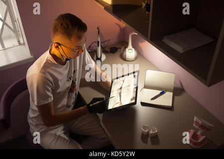 Dental doctor sits near work desk and looks x-ray on tablet computer in dental office. Stock Photo