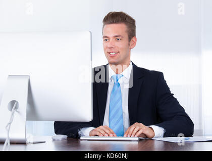 Portrait Of Happy Young Businessman Using Computer In Office Stock Photo