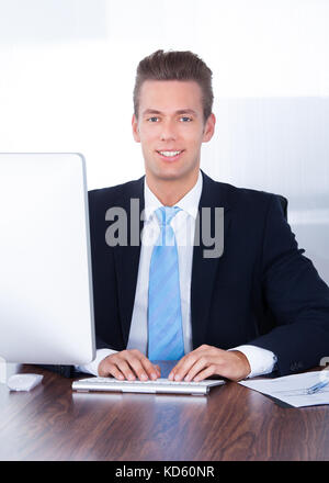 Portrait Of Happy Young Businessman Using Computer In Office Stock Photo