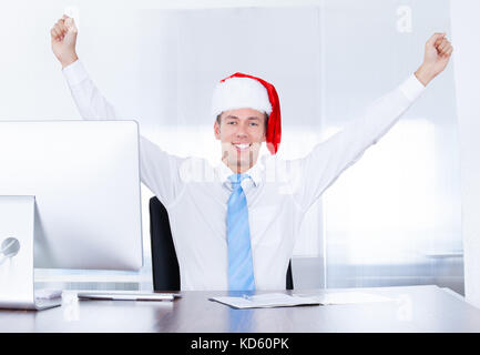 Happy Young Businessman Wearing Santa Hat Using Computer In Office Stock Photo