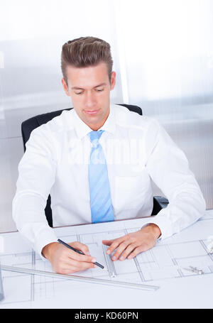Portrait Of Young Male Architect Working With Blueprint At Desk Stock Photo