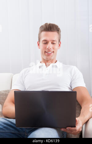 Portrait Of Happy Young Man Sitting On Couch Using Laptop Stock Photo
