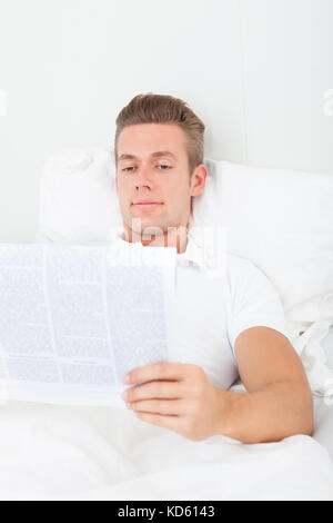 Portrait Of Young Man Lying On Bed Reading Newspaper Stock Photo