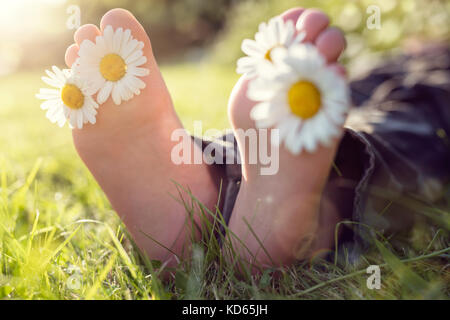 Child with daisy between toes lying in meadow relaxing in summer sunshine Stock Photo
