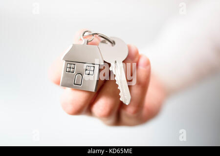 Holding house keys on house shaped keychain concept for buying a new home Stock Photo