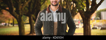 Portrait of young man with hands in pockets posing against white background against footpath amidst trees at park Stock Photo