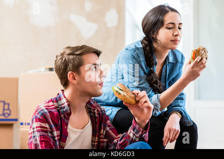 Young couple looking tired while eating a sandwich during break  Stock Photo