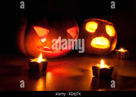 Scary halloween pumpkin and melon jack-o-lanterns on black background lit with small round and star candles. Selective focus, bokeh. Stock Photo