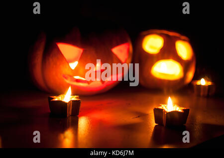 Scary halloween pumpkin and melon jack-o-lanterns on black background lit with small round and star candles. Selective focus, bokeh. Stock Photo