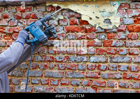 Worker with electrical hammer cleaning red brick wall outdoor Stock Photo