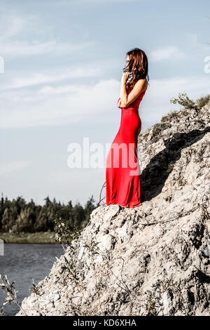 Lady in a red dress staying on the river edge Stock Photo