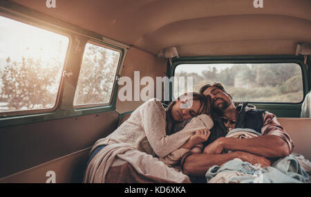 Friends sleeping together in van on road trip. Man and woman asleep in back seat of car. Stock Photo