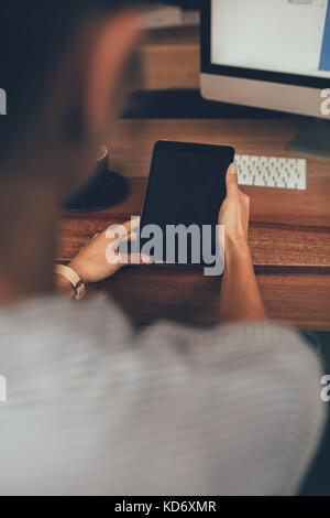 Over the shoulder view of woman sitting at desk and using digital tablet. Focus on tablet computer in female hands. Stock Photo